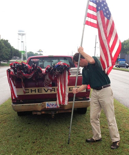 Kiwanis Club President Craig Schumacher places a flag in the ground along Highway 80 for Independence Day.